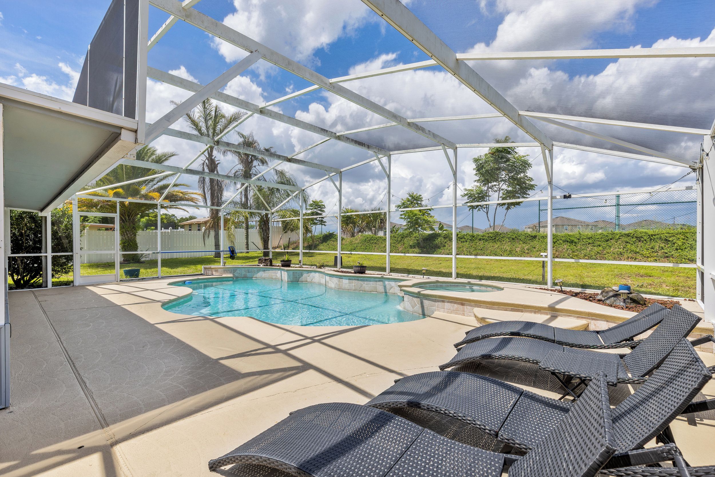 An outdoor swimming pool area with a covered section, lounge chairs, and a view of the surrounding landscape.