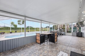 A covered outdoor area with a pool, seating, and a grill.
