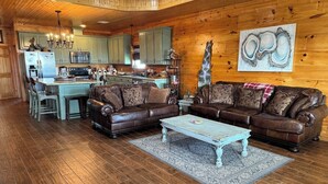 A cozy cabin interior with a wooden interior, a dining area, and a living room featuring a brown leather sofa set.