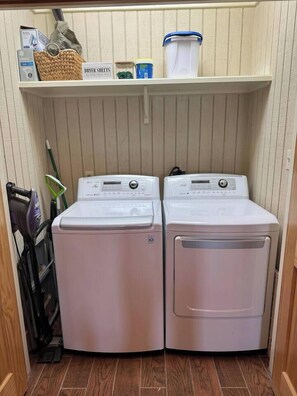 Une buanderie équipée de deux machines à laver à chargement frontal, d’une étagère contenant des produits de lessive et d’un étendoir.