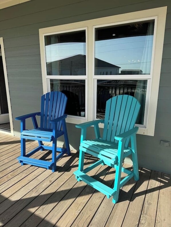 Deux fauteuils Adirondack sont placés sur une terrasse en bois devant une maison dotée de grandes fenêtres.