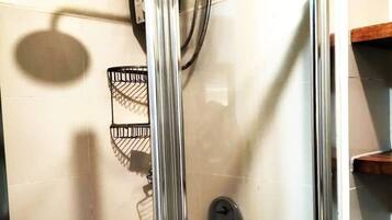 A glass-enclosed shower with a handheld showerhead and a handheld shower attachment.