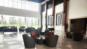 Een ruime lobby met een hoge plafond, grote ramen en diverse zitmogelijkheden, zoals banken en stoelen.