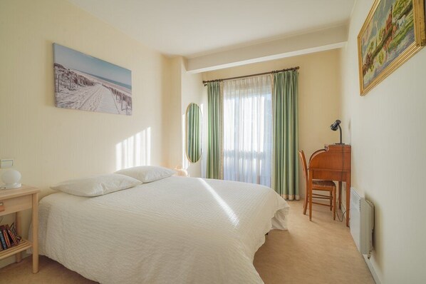 A bedroom with a large bed, a desk with a chair, a radiator, and a painting on the wall.