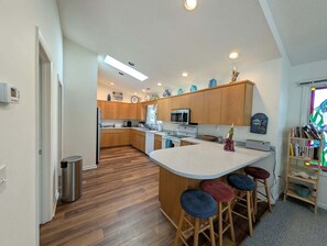A modern kitchen with wooden cabinets, a central island with stools, a microwave, and a sink.