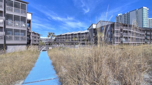 A pathway leading to a modern building complex with multiple balconies and a clear blue sky.
