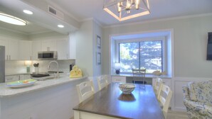 A modern kitchen with white cabinets, a dining table with chairs, and a window with blinds.