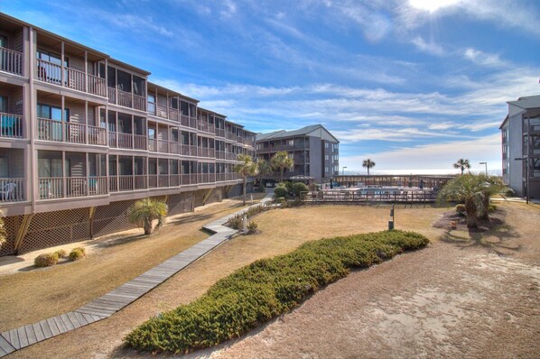 A multi-story hotel with balconies, a pool area, and a beach view.