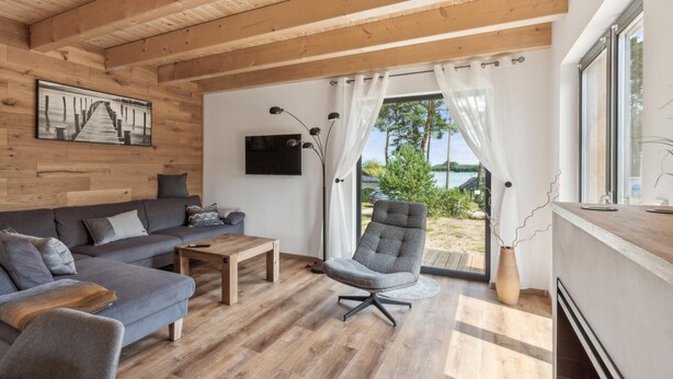 A modern living room with a wooden ceiling, a grey sofa, a wooden coffee table, and a grey armchair.