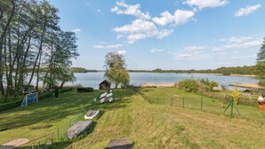 A grassy area with a small pond, a wooden structure, and a fenced area with a view of a lake and distant hills.