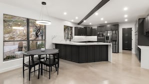 Een moderne keuken met donkere kastjes, een centraal eiland en een eetgedeelte met een ronde tafel en stoelen.