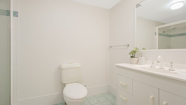 A bathroom with a toilet, a sink, a mirror, and a shower area. - Sunrise Sea 8 - In the Heart of Coolangatta - Min. 3 Night Stays! (Coolangatta)