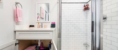 Un baño con ducha, tocador con espejo y barra para toallas.