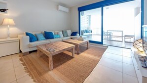 A modern living room with a white sofa, blue cushions, a wooden coffee table, and a large glass door leading to an outdoor area. - 2 bedroom nice apartment in Moncofa (Moncofa)