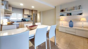 A modern kitchen with white cabinets, a microwave, and a stove. There is a dining table with chairs and a decorative bowl. The room has a tiled floor and a shelf with decorative items. - 2 bedroom nice apartment in Moncofa (Moncofa)