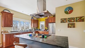 A modern kitchen with wooden cabinets, a large island, and a stainless steel range hood. - Cody's Clubhouse: 3 br, wood fireplace, firepit & deck (Waterbury Center)