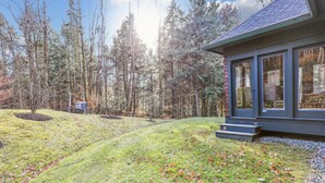 A modern house with a large glass window, surrounded by a forest. - Cody's Clubhouse: 3 br, wood fireplace, firepit & deck (Waterbury Center)