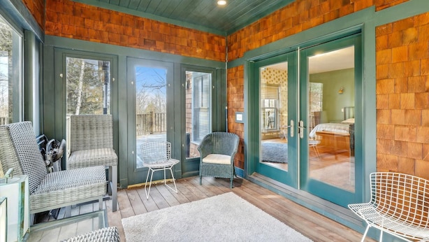 A cozy room with wicker chairs, a wooden floor, and a large window. - Cody's Clubhouse: 3 br, wood fireplace, firepit & deck (Waterbury Center)