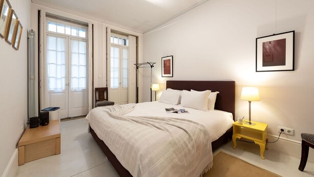 Une chambre à coucher avec un grand lit, des lampes de chevet, une petite table et une fenêtre avec des rideaux.