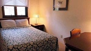 Un dormitorio con cama, una mesita de noche con lámpara, una silla y un cuadro enmarcado en la pared.
