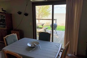 A dining area with a table set for two, a view of a deck and outdoor space, and a wooden cabinet with a bird perched on top. - House #133 Cozy 3 bedroom Family home with Spectacular views. (Huron)