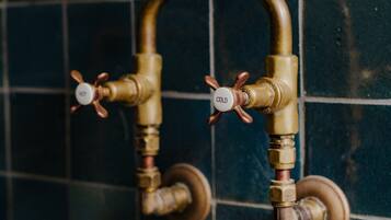 A bathroom with a tiled wall and two brass faucets with temperature control knobs.