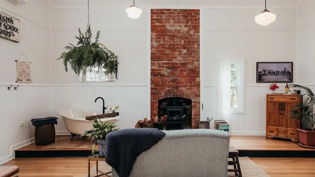 Una sala de estar acogedora con chimenea de ladrillo, una bañera blanca y plantas colgantes.