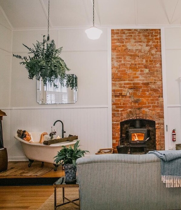 A cozy living room with a brick fireplace, a clawfoot bathtub, and a hanging plant.