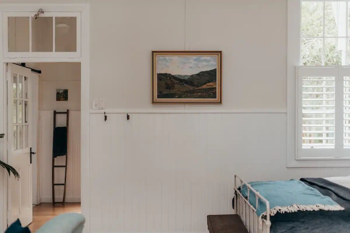 A bedroom with a bed, a window with blinds, a door, and a wall-mounted picture.