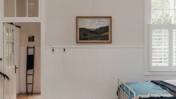 A bedroom with a bed, a window with blinds, a door, and a wall-mounted picture.