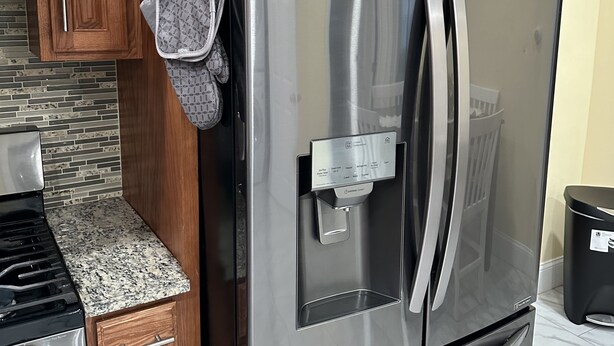 A stainless steel refrigerator with a water dispenser, wooden cabinets, a granite countertop, and a black trash can. - Charming quiet (Manchester)