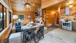 A cozy cabin interior with a dining area, a fireplace, and a kitchen.