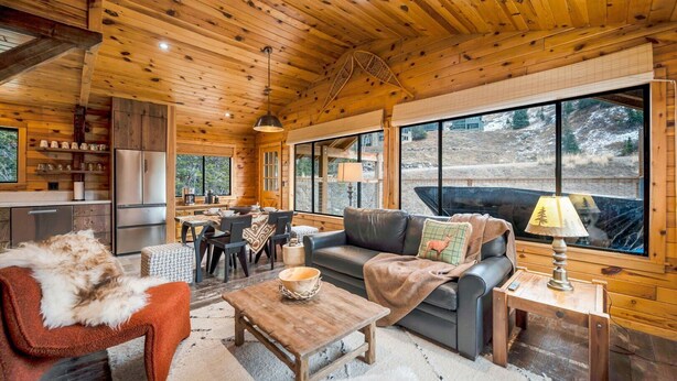 A cozy cabin interior with a dining area, a sofa, and a fireplace.