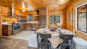 A wooden cabin interior with a kitchen, dining area, and large windows.