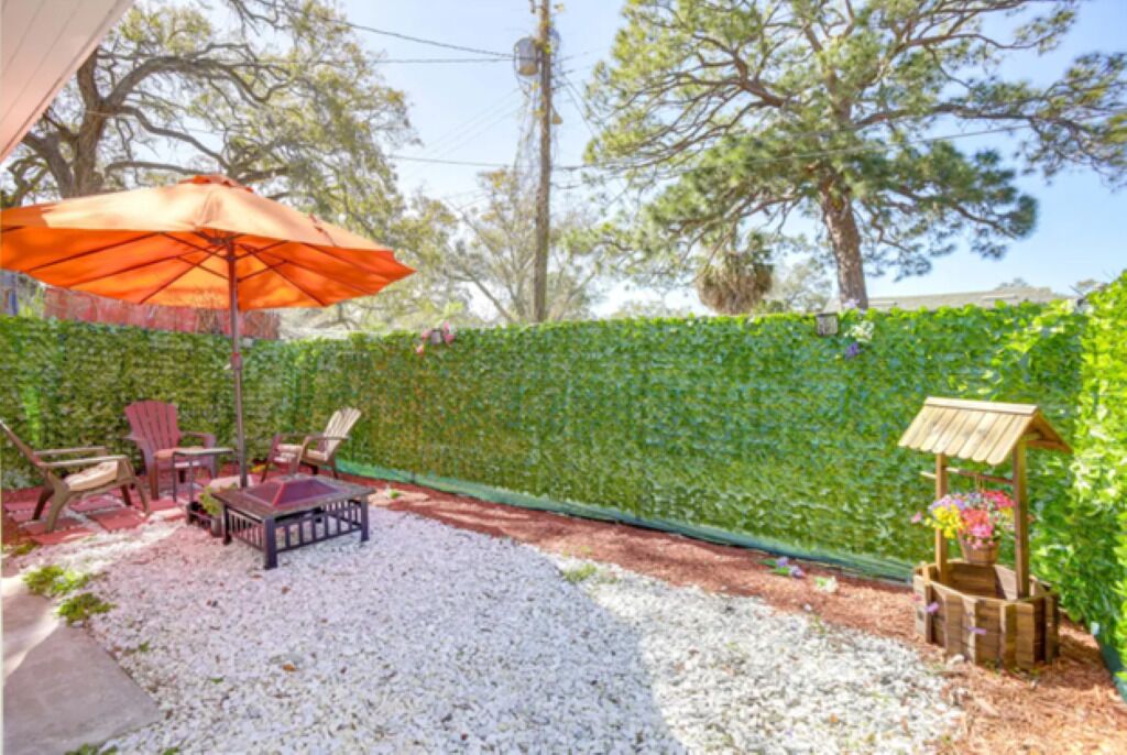 Une terrasse extérieure avec un espace salon, une table en bois et un parasol orange.