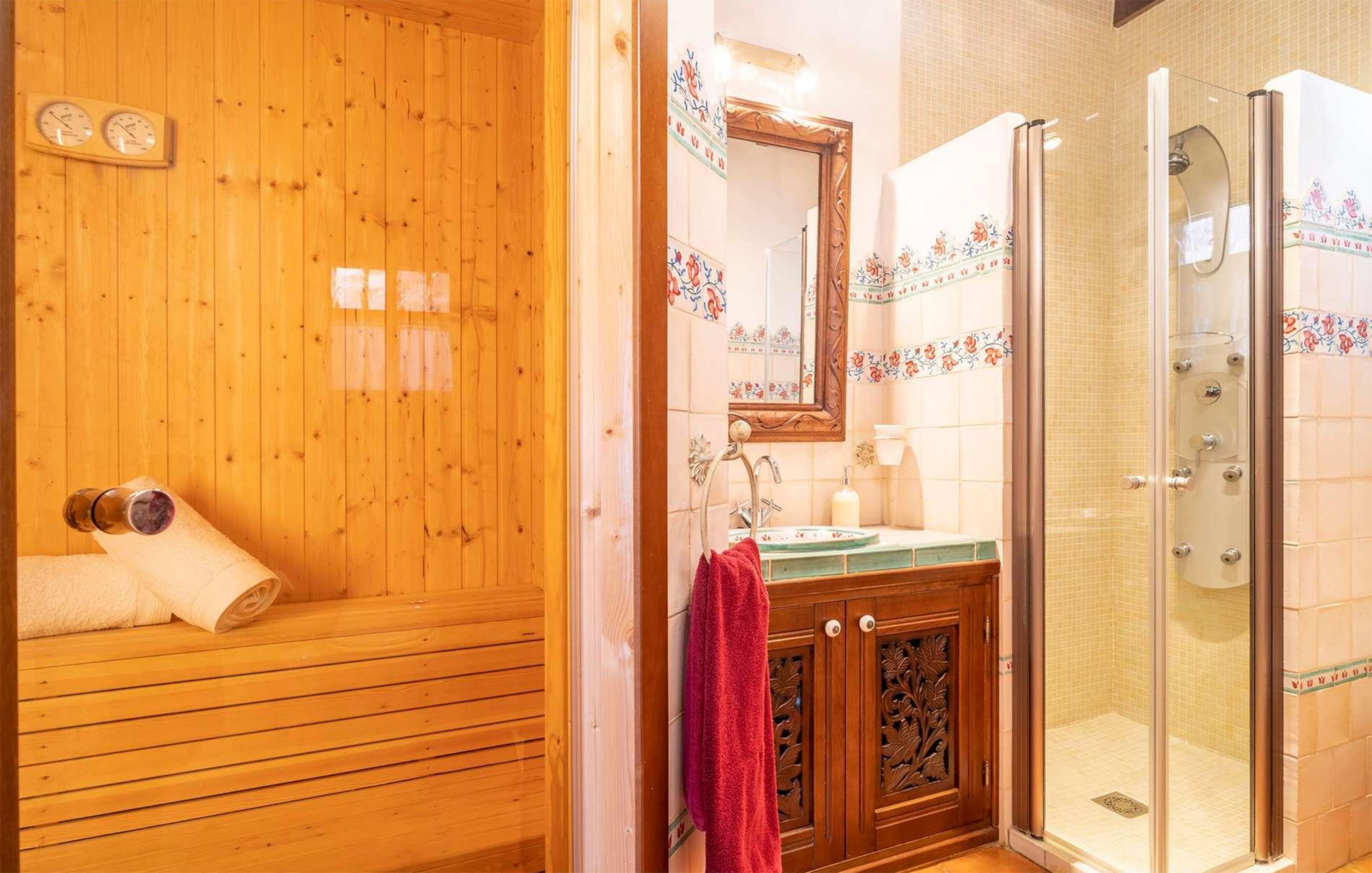 A wooden sauna with towels and bottles, a wooden cabinet with a mirror, and a glass-enclosed shower area.