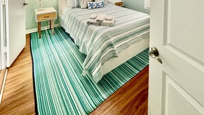 Un dormitorio con cama, mesita de noche, lámpara, ventilador de techo y alfombra a rayas.