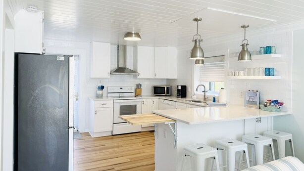 Cocina moderna con armarios blancos, electrodomésticos de acero inoxidable y una isla de madera con taburetes de bar.