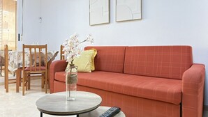 Ein Wohnzimmer mit einem roten Sofa, einem runden Tisch mit einer Vase und einer Fernbedienung.
