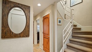 Un pasillo con una puerta de madera, un espejo redondo y una escalera con alfombra.