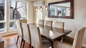 Comedor con mesa de madera y seis sillas, ventanas amplias y un espejo fijado a la pared.