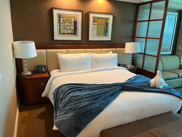 A hotel room with a bed, two bedside lamps, a nightstand, a chair, and artwork on the wall.
