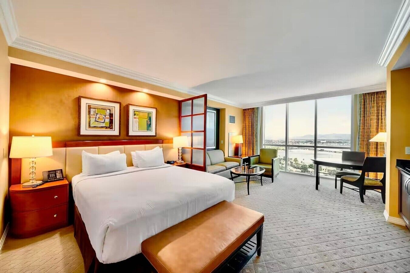 A hotel room with a large bed, a desk, a chair, a sofa, and a view of the city.