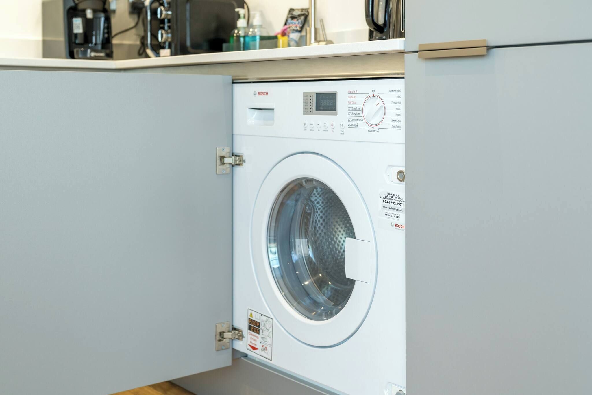 Un lave-linge Bosch dans une cuisine moderne, avec un meuble blanc au-dessus.
