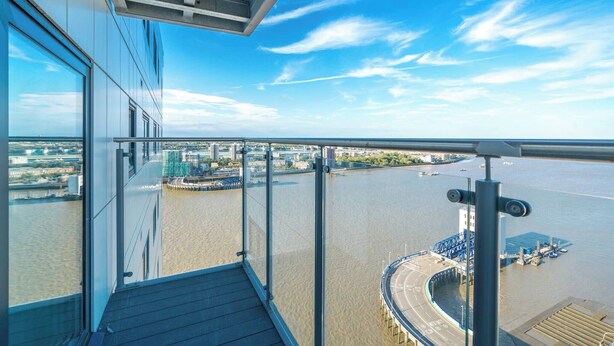 A high-rise building with a glass balcony overlooking a river, a bridge, and a cityscape. - Skyvillion - River Thames Apt Nr Excel o2 City Ap (London)