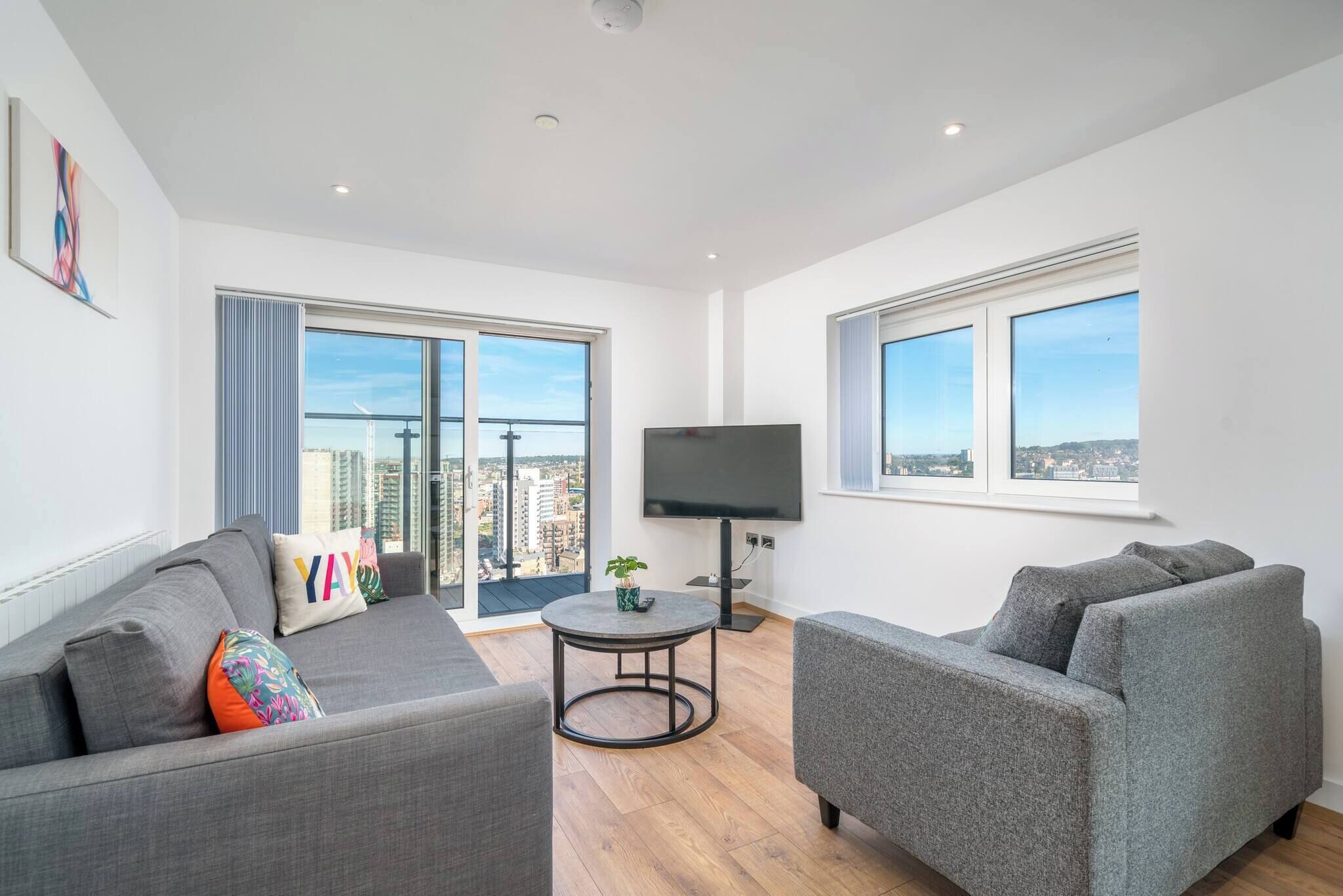 A modern living room with a grey sofa, a grey armchair, a round coffee table, and a flat-screen TV.