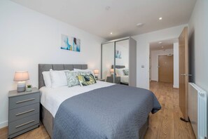 A bedroom with a bed, bedside tables, a wardrobe, and a painting on the wall. - Skyvillion - River Thames Apt Nr Excel o2 City Ap (London)