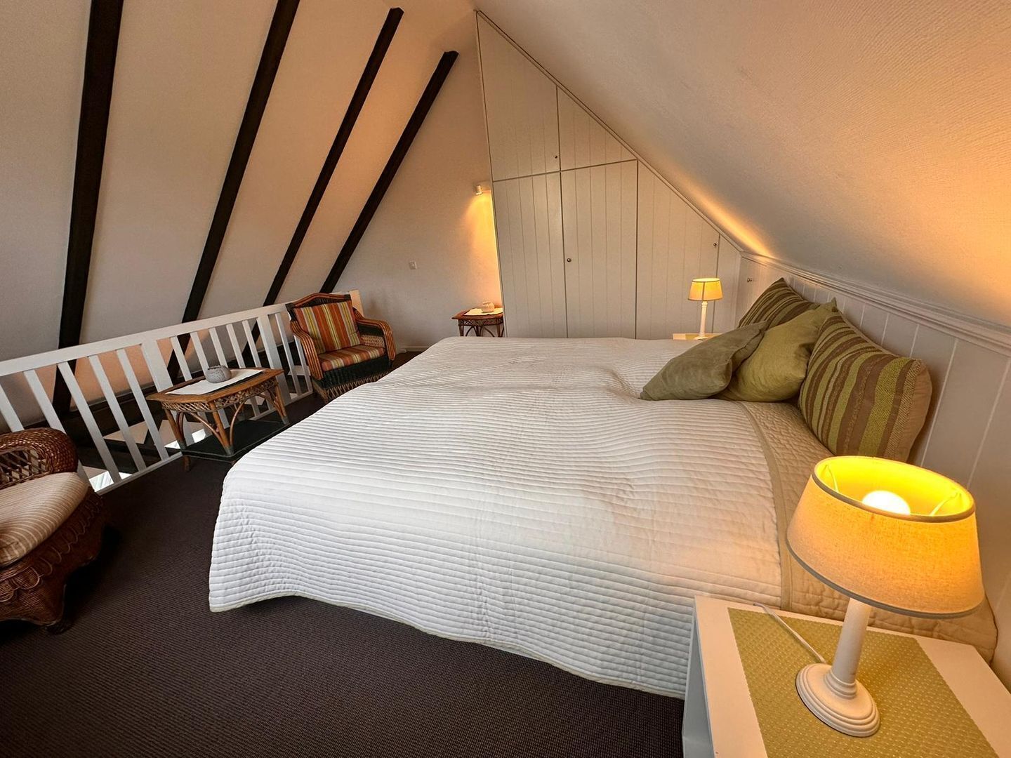 A bedroom with a large bed, a nightstand with a lamp, a chair, and a small table.