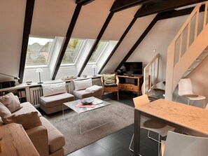 A modern loft-style living room with a sloped ceiling, large windows, a sofa set, a coffee table, a TV, and a dining area. - Ruhig im Inseldorf Nieblum Gelegen - Ferienanlage Bi de Süd 43 (Nieblum)