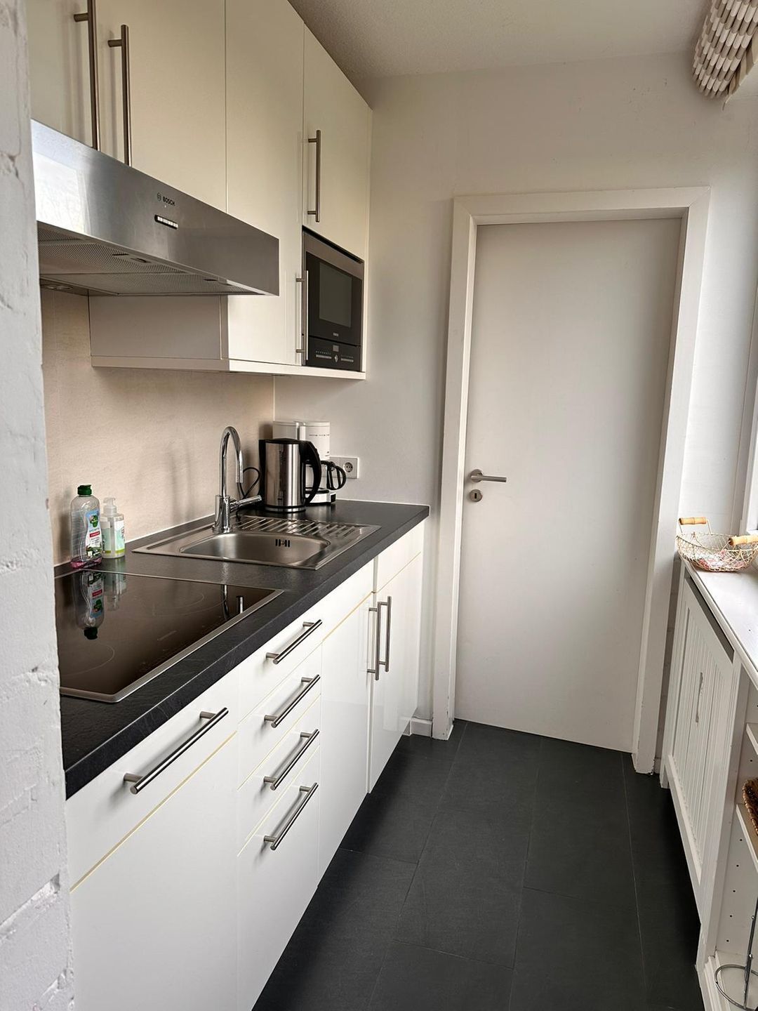 A compact kitchen with a black countertop, stainless steel appliances, and white cabinetry.
